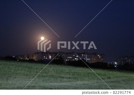 the moon on the outskirts of the city at night under the light of lanterns. night city landscape moon over grass 82291774