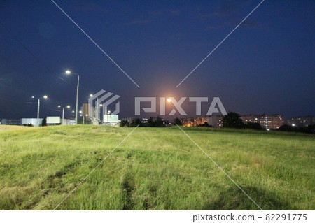 the moon on the outskirts of the city at night under the light of lanterns. night city landscape moon over grass 82291775