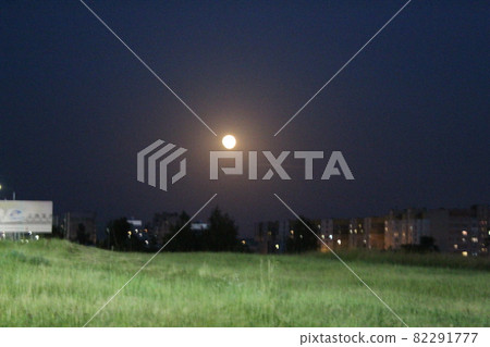 the moon on the outskirts of the city at night under the light of lanterns. night city landscape moon over grass 82291777