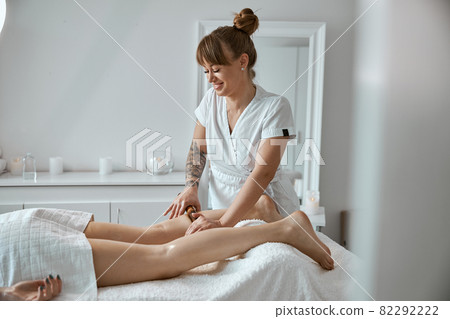 Conident female specialist is doing leg massage with bamboo stick to beautiful caucasean woman client Conident female specialist is doing leg massage with bamboo stick to beautiful caucasean woman client 82292222