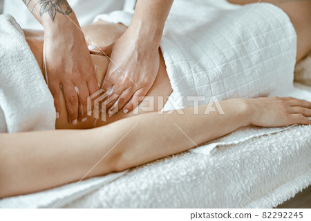 Professional massagist is doing stomach massage to young female client in modern wellness salon Professional massagist is doing stomach massage to young female client in modern wellness salon 82292245