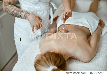 professional female specialist is doing cupping therapy on the back of beautiful caucasian lady professional female specialist is doing cupping therapy on the back of beautiful caucasian lady 82292248