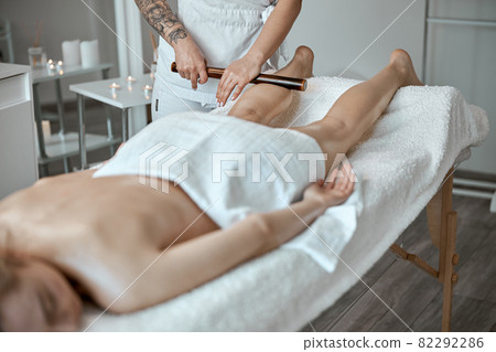 Conident female specialist is doing leg massage with bamboo stick to beautiful caucasean woman client 82292286