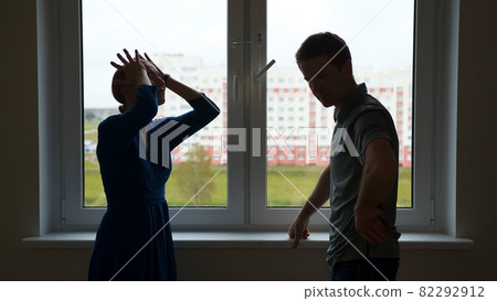 Quarantine concept. Silhouette of young spouses swearing on the background of the window of their apartment. Quarantine concept. Silhouette of young spouses swearing on the background of the window of their apartment. 82292912