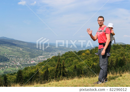 Family hiking in nature. A father carries his son in a backpack high among the hills and forest. 82296012