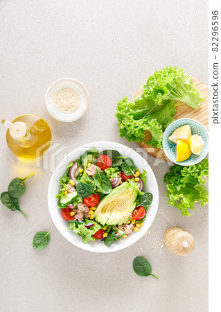 Avocado and tuna fresh vegetable salad with tomato, cucumber corn, onion, lettuce and spinach. Healthy and detox food concept. Ketogenic diet. Buddha bowl dish on light background, top view 82296596