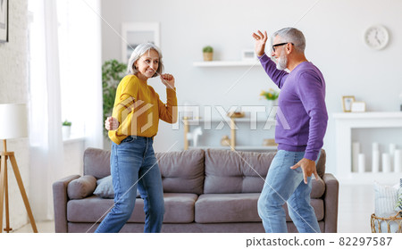Energetic senior family couple dancing together in living room at home, moving to music 82297587