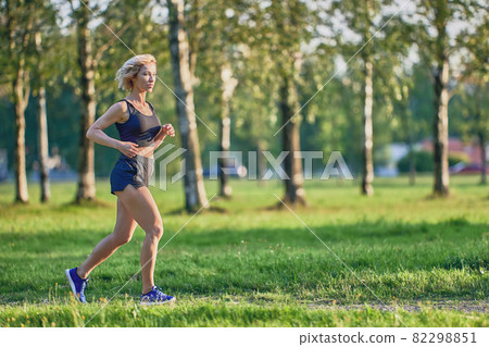 Jogging in park by slender woman in sportswear at summer day. Jogging in park by slender woman in sportswear at summer day. 82298851
