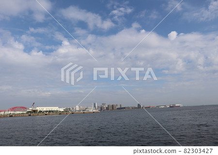 Clouds of various colors and shapes, blue sky, sea, red bridges, a city with many buildings on an artificial island, a jetty and a view of tankers 82303427
