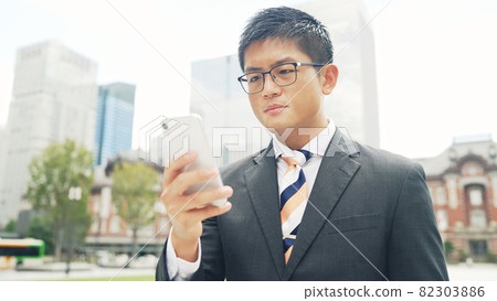A businessman looking at a smartphone in the city A businessman looking at a smartphone in the city 82303886