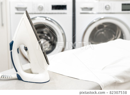 Iron on ironing board with white shirt in laundry room Iron on ironing board with white shirt in laundry room 82307538