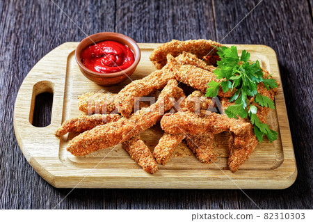 crunchy Baked Chicken Tenders on a wooden board 82310303