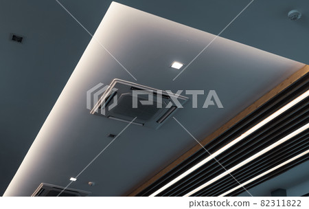 Selective focus on cassette type air conditioner mounted on ceiling wall. Air duct on ceiling in hotel. Air heading unit on gypsum wall. Cool system in the building. Air flow and ventilation system. 82311822
