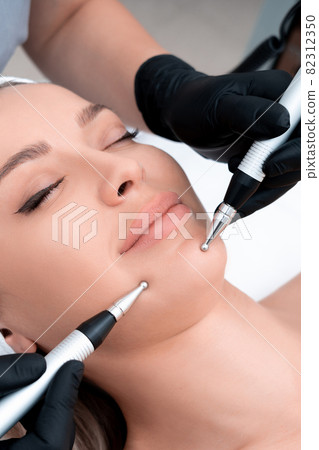 Cosmetology. Beautiful Woman At Spa Clinic Receiving Stimulating Electric Facial Treatment From Therapist. Closeup Of Young Female Face During Microcurrent Therapy Cosmetology. Beautiful Woman At Spa Clinic Receiving Stimulating Electric Facial Treatment From Therapist. Closeup Of Young Female Face During Microcurrent Therapy 82312350