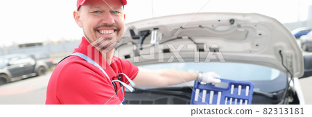 Portrait of young smiling car repairman with set of tools on hood of car Portrait of young smiling car repairman with set of tools on hood of car 82313181