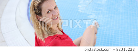 Young smiling woman is sitting on edge of pool 82313228