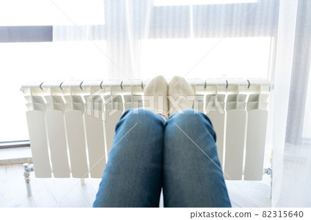 Woman warming up with feet on heater wearing woolen socks 82315640