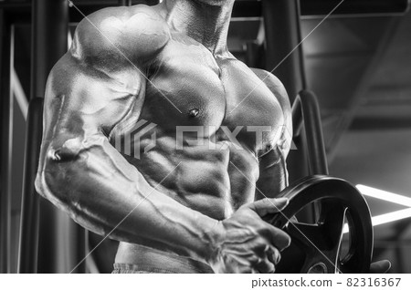 Young athletic man pumping up muscles in the gym at workout. Sport and health care concept background 82316367