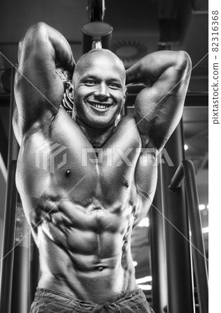 Young athletic man pumping up muscles in the gym at workout. Sport and health care concept background Young athletic man pumping up muscles in the gym at workout. Sport and health care concept background 82316368