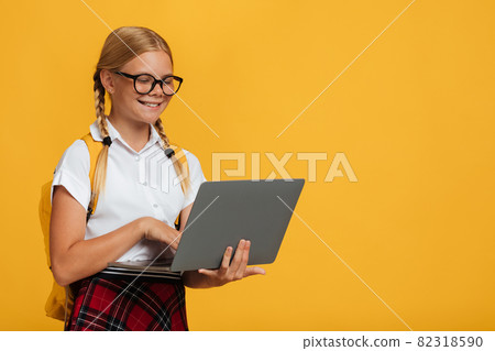 Cheerful smart caucasian young girl student in glasses studying with laptop, isolated on yellow background Cheerful smart caucasian young girl student in glasses studying with laptop, isolated on yellow background 82318590