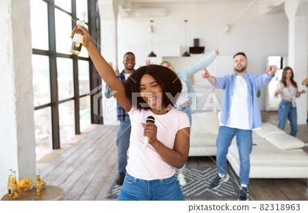 Millennial black lady with beer bottle and mic singing karaoke with diverse friends at home Millennial black lady with beer bottle and mic singing karaoke with diverse friends at home 82318963