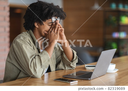 Tired Black Guy Suffering Eyesight Problem While Working On Laptop In Cafe 82319089