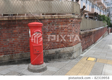 A view of the red round post in front of the brick wall and the slope of the cobblestone sidewalk 82319958