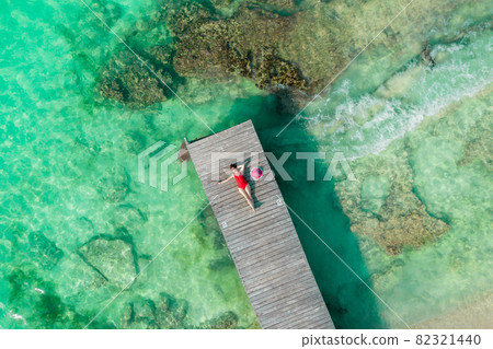 Aerial view of woman laying on wooden pier at sunny summer day in Cancun, Mexico, top view. Young sexy woman in the red swimsuit in summertime in Caribbean. Summer beach vacation concept 82321440