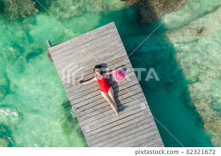 Aerial view of woman laying on wooden pier at sunny summer day in Cancun, Mexico, top view. Young sexy woman in the red swimsuit in summertime in Caribbean. Summer beach vacation concept Aerial view of woman laying on wooden pier at sunny summer day in Cancun, Mexico, top view. Young sexy woman in the red swimsuit in summertime in Caribbean. Summer beach vacation concept 82321672