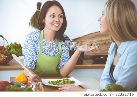 Two women friends taste new recipes for delicious fresh salads while sitting at the kitchen table. Vegetarian cooking concept Two women friends taste new recipes for delicious fresh salads while sitting at the kitchen table. Vegetarian cooking concept 82321719