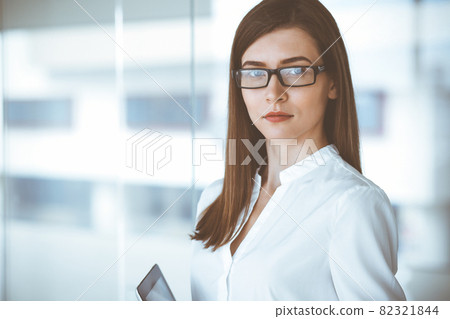 Beautiful female specialist with tablet computer standing in modern office and smiling charmingly. Working on design, data analysis, plan strategy. Business people concept Beautiful female specialist with tablet computer standing in modern office and smiling charmingly. Working on design, data analysis, plan strategy. Business people concept 82321844