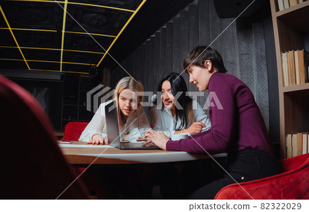 Three young business women sitting at table with laptop and working on a project in cafe. Teamwork, business meeting. Freelancers working. 82322029