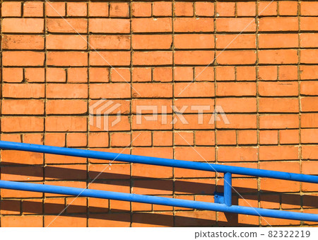 Orange brick wall. Textured background with copy space for design work. Material pattern. Reddish-brown brick blocks facade with blue handrail. Industrial wallpaper with brickwork. No people Orange brick wall. Textured background with copy space for design work. Material pattern. Reddish-brown brick blocks facade with blue handrail. Industrial wallpaper with brickwork. No people 82322219