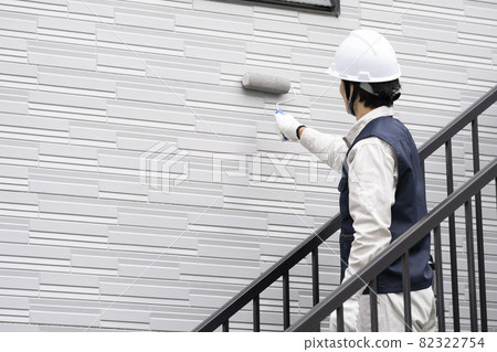 A painter who paints the exterior walls of a detached house with a roller 82322754