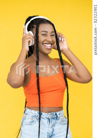 Enjoying music. Audio device. Digital technology. Happy smiling Afro woman listening to song in earphones isolated on yellow background. Enjoying music. Audio device. Digital technology. Happy smiling Afro woman listening to song in earphones isolated on yellow background. 82322901