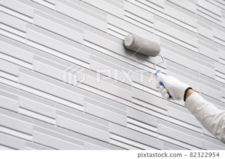 At hand of a painter who paints the outer wall of a detached house with a roller 82322954