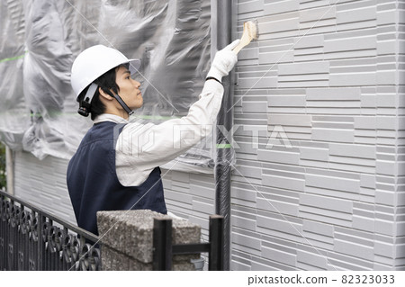 A painter who paints the exterior walls of a detached house with a roller 82323033