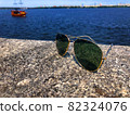 Fashionable aviator sunglasses with dark lenses and gold frames sit on a granite stone pier and reflect the sun's rays. In the background, a pirate ship with tourists floats on the Dnieper River 82324076