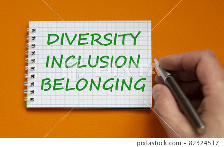 Diversity, inclusion, belonging symbol. Businessman writing words 'Diversity, inclusion, belonging' on white note, orange background. Business, diversity, inclusion, belonging concept. Copy space. Diversity, inclusion, belonging symbol. Businessman writing words 'Diversity, inclusion, belonging' on white note, orange background. Business, diversity, inclusion, belonging concept. Copy space. 82324517