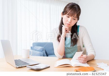 A woman who keeps a household account book while checking the receipt and is worried about making ends meet A woman who keeps a household account book while checking the receipt and is worried about making ends meet 82325347