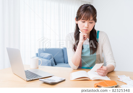 一位女士一邊查看收據一邊保留家庭賬簿,擔心入不敷出 一位女士一邊查看收據一邊保留家庭賬簿,擔心入不敷出 82325348