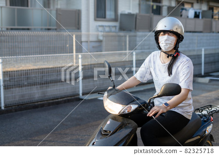 A woman wearing a mask and riding a scooter bike 82325718