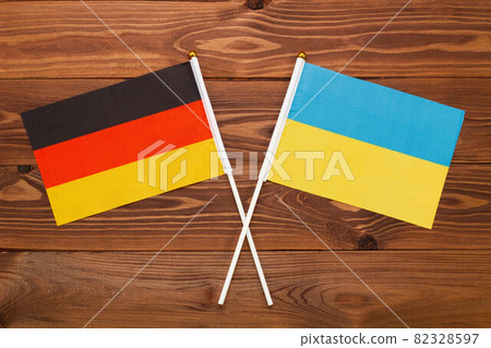 The flag of Germany and the flag of Ukraine are crossed with each other on a brown background with a wood texture. Top view. Close Up 82328597