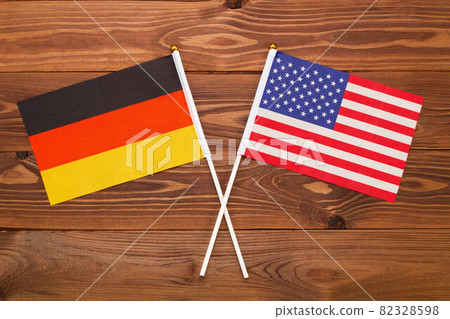 The flag of Germany and the flag of USA are crossed with each other on a brown background with a wood texture. Top view. Close Up 82328598