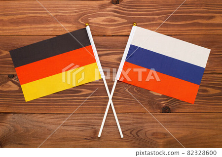 The flag of Germany and the flag of Russia are crossed with each other on a brown background with a wood texture. Top view. Close Up The flag of Germany and the flag of Russia are crossed with each other on a brown background with a wood texture. Top view. Close Up 82328600