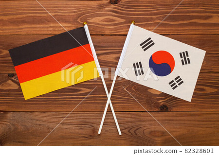 The flag of Germany and the flag of South Korea are crossed with each other on a brown background with a wood texture. Top view. Close Up The flag of Germany and the flag of South Korea are crossed with each other on a brown background with a wood texture. Top view. Close Up 82328601