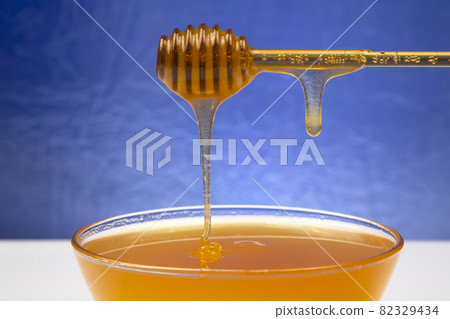 fresh honey dripping from a spoon into a plate on a blue background. organic vitamin health food 82329434