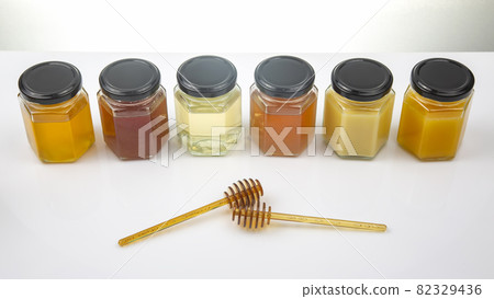 Hexagonal jars with different types and colors of fresh flower honey and a honey spoon 82329436