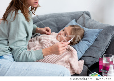 Mom sits next to her daughter and looks at the thermometer after taking her temperature Mom sits next to her daughter and looks at the thermometer after taking her temperature 82332356