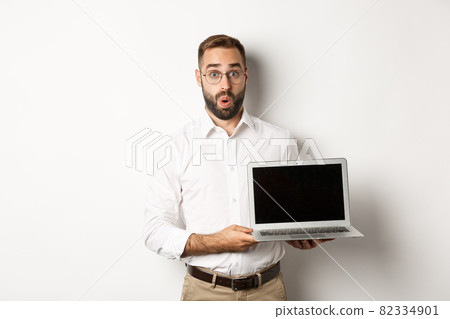 Amazed businessman showing laptop screen, standing against white background 82334901